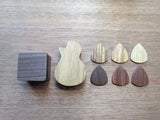 Square and small guitar shaped pick boxes next to wooden guitar picks